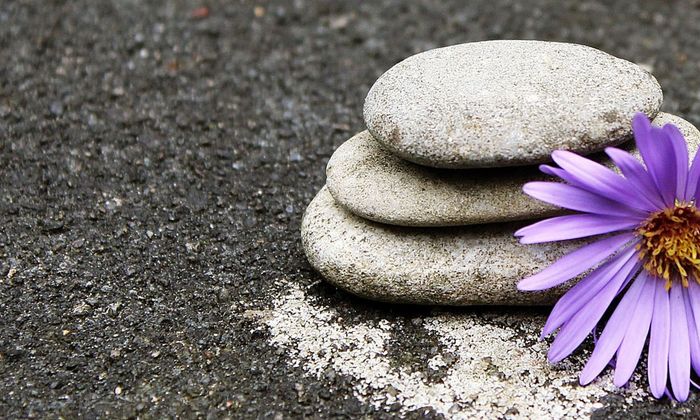 3 Steine aufeinander mit lila Blume daneben
